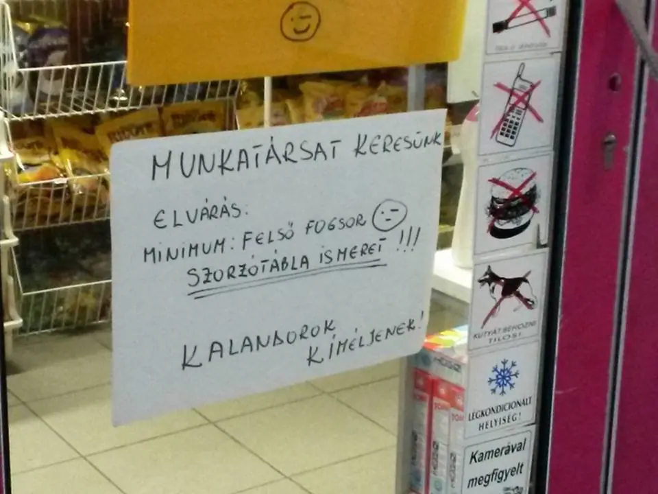 Üzletajtóra ragasztott kézzel írt munkatárskereső tábla a szorzótábla ismeretét kiemelő humoros szöveggel