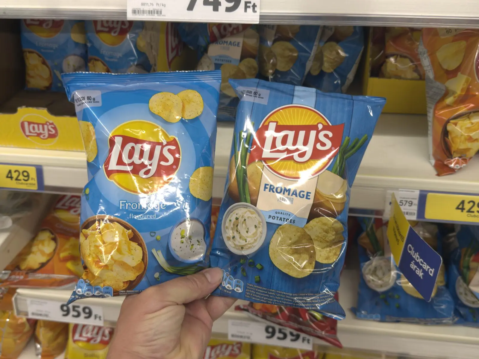 Két eltérő grafikájú Lay’s Fromage chipses zacskó egymás mellett egy üzleti polc előtt